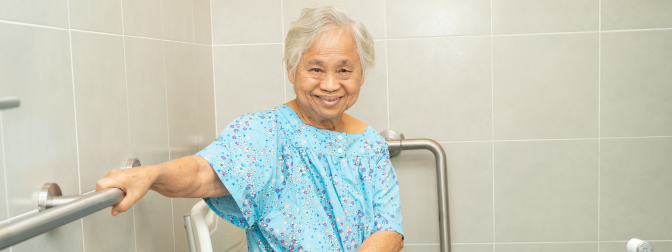 Idosa sorrindo em banheiro adaptado com barras de apoio, representando segurança e acessibilidade no banho para pessoas com mobilidade reduzida