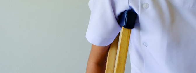 Pessoa utilizando uma muleta apoiada na axila, vestindo camisa branca, representando mobilidade assistida.